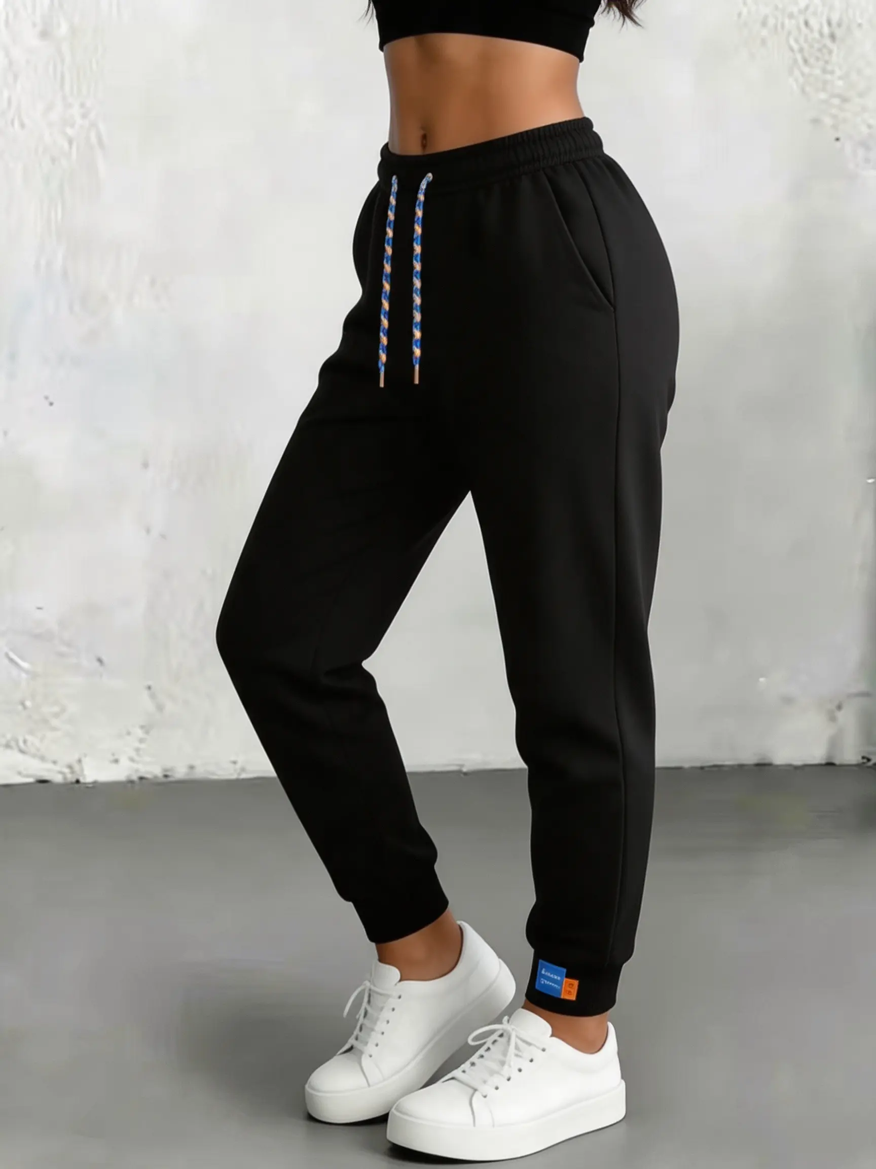 Women’s black sporty jogger sweatpants, color‑blocked woven design, elastic high waist with drawstring, slimming fit, ankle cuffs with small logo detail, drapey fabric, versatile casual long pants for a hot‑girl look.