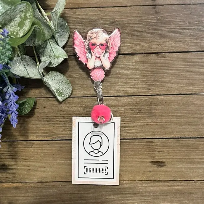 Valentine-themed badge reel with a pink angel, pom-pom accent, and heart charm. Lightweight, fun, and full of love.