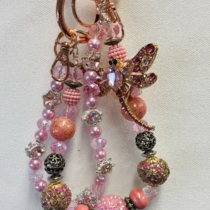 Handcrafted fancy beaded dragon fly keychain/phone charm/bagcharm with pink glass crystal beads accents and luxury spacers. Acrylic beads and soft pink pearl like beads. Rose gols color oring with split keyring and hook attached.  Phone card attachment