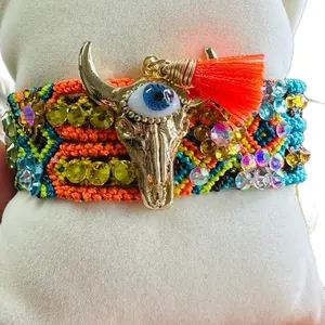 The adjustable woven bracelet features a cow horn charm with a glass eye design and attached rhinestones.