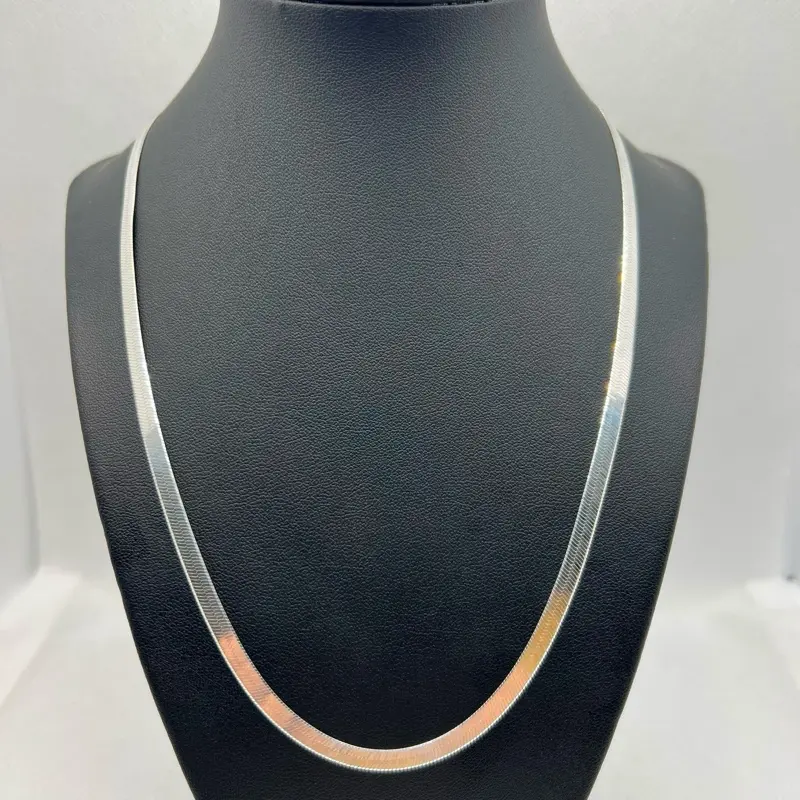 The centerpiece on display is an elegant 925 sterling silver herringbone chain necklace, characterized by its fluid, flat, V-shaped links that intensely reflect the light. Size 22 in weight 12 grams wide 4.3 mm