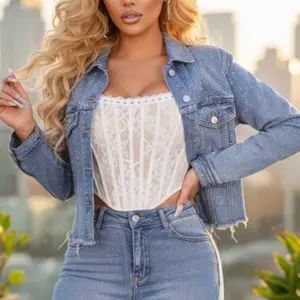 Jacklyn Jacket - Cropped denim jacket featuring allover rhinestone stud detailing for a subtle sparkle. Designed with a classic collar, long sleeves, button-front closure, and functional chest flap pockets. Finished with a raw frayed hem for an edgy touch